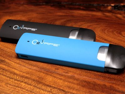 2 Traveler Extreme ® Vari-Vape Pens are displayed horizontally at an angle. The pen in the back is black, with the blue pen in front. The O2VAPE logo is displayed on the body of both pens.