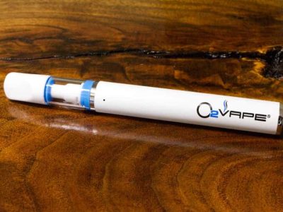 A single Traveler Extreme XL Full Ceramic vape pen is pictured laying horizontally across a warm wood surface. The pen is white, with a visible O2VAPE logo on the body. A slim silver disc is visible at the base.