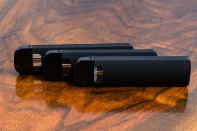 3 black Traveler Extreme Vari-Vape pens standing on their side and arranged in an offset lineup, with the mouthpieces on the left against a warm wood surface.