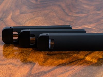 3 black Traveler Extreme Vari-Vape pens standing on their side and arranged in an offset lineup, with the mouthpieces on the left against a warm wood surface.