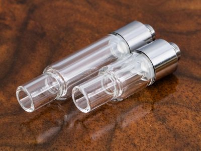 Two All Glass 510 Vape Cartridges are pictured against a warm brown marble surface, displayed at a right angle with the glass mouthpiece at one end, and the base at the other end. The 1ml cartridge on the left is longer, while the smaller .5ml cartridge is on the right.